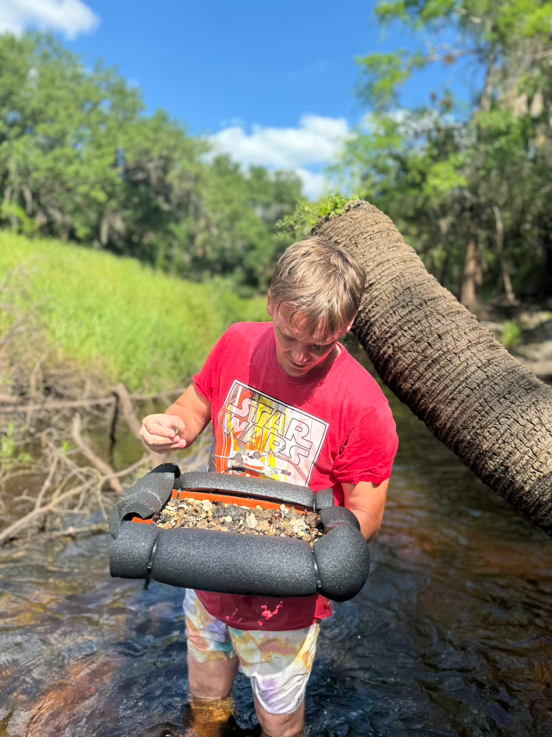 standing in a river screening for fossils